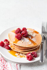 Stack of pancakes with raspberry, almonds and maple syrup on white plate. Breakfast food.