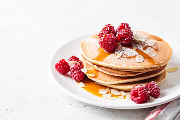 Stack of pancakes with raspberry, almonds and maple syrup on white plate. Breakfast food.