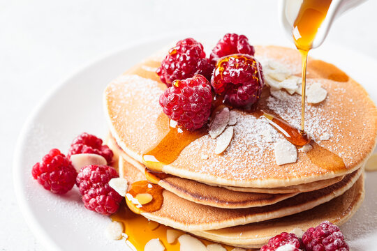 Stack of pancakes with raspberry, almonds and maple syrup on white plate. Breakfast food.