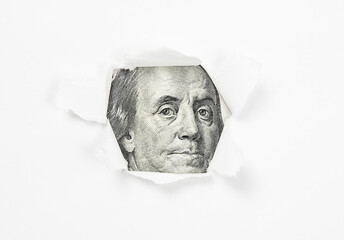 Benjamin Franklin portrait on dollar bill in torn paper hole. Business concept