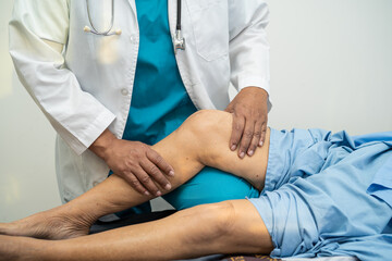 Asian doctor physiotherapist examining, massaging and treatment knee and leg of senior patient in...