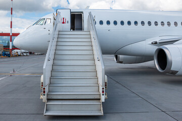 Fototapeta na wymiar White passenger aircraft with a boarding steps on the airport apron