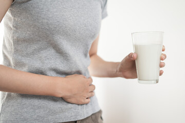 Slim woman hand touch stomach as stomachache and pain holding a glass of milk as dairy intolerant lactose intolerance allergy health care concept