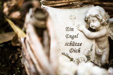 Engelchen mit Schrift "Ein Engel schütze dich" auf einem Grab