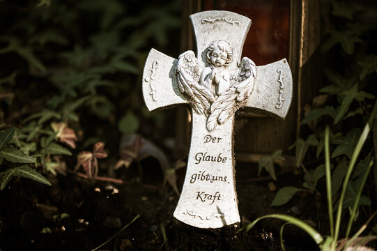 Steinkreuz mit Engelchen auf einem Grab mit Schrift "Der Glaube gibt uns Kraft"