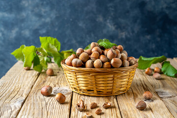 Hazelnuts in basket with leaves on wooden rustic table and dark grey background