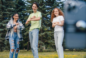 Group of three influencers shooting dance video for social network on cellphone, having fun outdoors. Millennial bloggers streaming content for their vlog