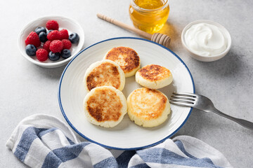 Cottage cheese fritters with berries, honey and yogurt, grey concrete background. Sweet breakfast food