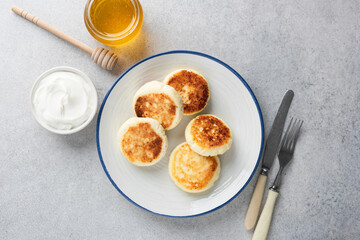 Syrniki, sweet curd cheese or ricotta cheese fritters on white plate, grey concrete background, top view