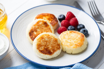 Cottage cheese fritters with berries and honey on plate, closeup view. Sweet breakfast food