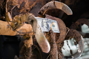 Hundred dollar bill between the teeth of a tractor rototiller close-up. Finance and agricultural...