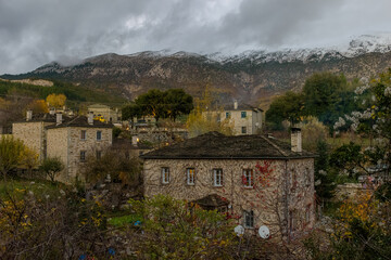 Fototapeta na wymiar Τraditional architecture with the stone buildings and snowy mountains as background during fall season in the picturesque village of papigo , zagori Greece