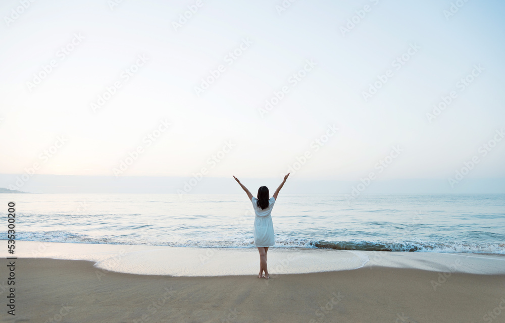 Wall mural Happy woman standing on the beach with hands up.