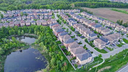 Aerial footage of Canadian town showing suburban housing estates in geometrical position and rows of houses. Summer golden hour evening with long shadows.