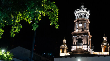 vista nocturna de torre de iglesia con corona en lo alto y arbol en primer plano, iglesia de...