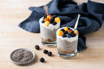 Chia pudding in jar with berries, fruits and granola layer on a wooden table background