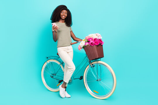 Full length portrait of adorable lovely girl hold telephone cycling fresh wildflowers isolated on aquamarine color background