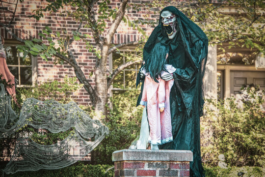 Evil undead creature in robe preparing to devour sleepwalking little girl- ghoulish Halloween decoration outdoors in front of house