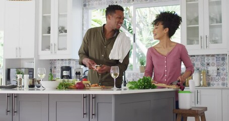 Happy african american couple cooking and drinking wine in kitchen