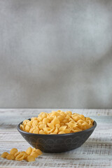 Deep bowl with raw pasta on wooden table. Raw pasta on a gray background.