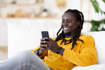 Black Guy Messaging With Friends Or Browsing Internet On Smartphone At Home
