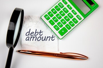 The words debt amount on crumpled paper next to a calculator and a magnifying glass. The concept of...