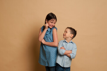 a dark-haired girl 9-12 years old and a boy 5-7 years old communicate on a beige background, communication between peers