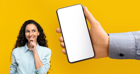 Smiling millennial middle eastern brunette lady think, look at huge smartphone with empty screen in hand