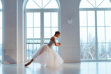 ballerina in long white tulle skirt, crouching in bow pose,