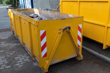 Reduced size of small and narrow yellow metal dumpsters container, construction trash, street reconstruction.