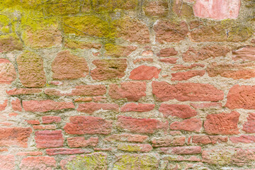 Mit Moos und Wurzeln bedeckte Mauer oder Wand  mit roten Steinen aus dem Mittelalter