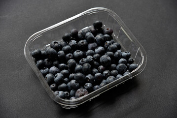 Fresh juicy blueberries Vaccinium myrtillus in a container on a black background.