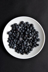 Black blueberries Vaccinium myrtillus on a white plate.
