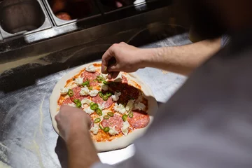 Fototapeten Pizza making process. Male chef hands making authentic pizza in the pizzeria kitchen. © arthurhidden