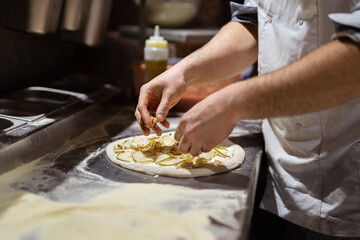 Pizza making process. Male chef hands making authentic pizza in the pizzeria kitchen. - obrazy, fototapety, plakaty