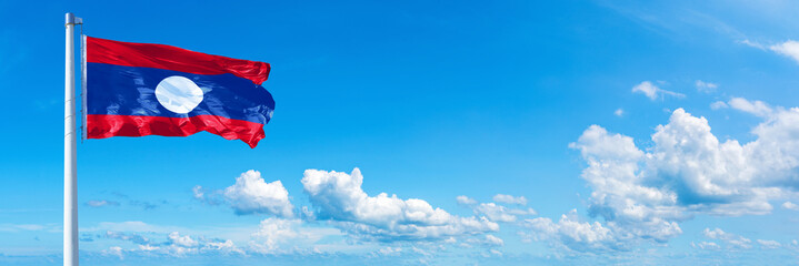 Laos flag waving on a blue sky in beautiful clouds - Horizontal banner