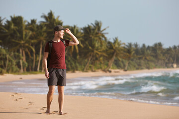 Happy man walking on idyllic sand beach against coast with palm trees in Sri Lanka..