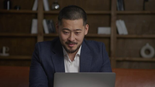 Asian businessman working hapy on his laptop computer in his loft office wearing a suit