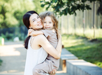 Fototapeta premium Happy summer time. Little daughter hugging her young happy mom in the park.