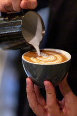 Barista preparing cafe latte, pouring milk into a coffee. Closeup on hands with latte art.