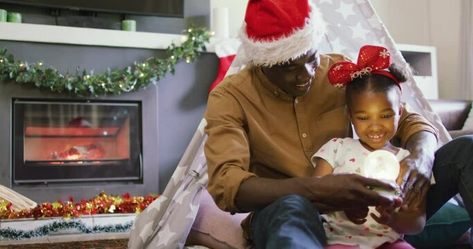 Happy african american father with daughter playing with snow globe