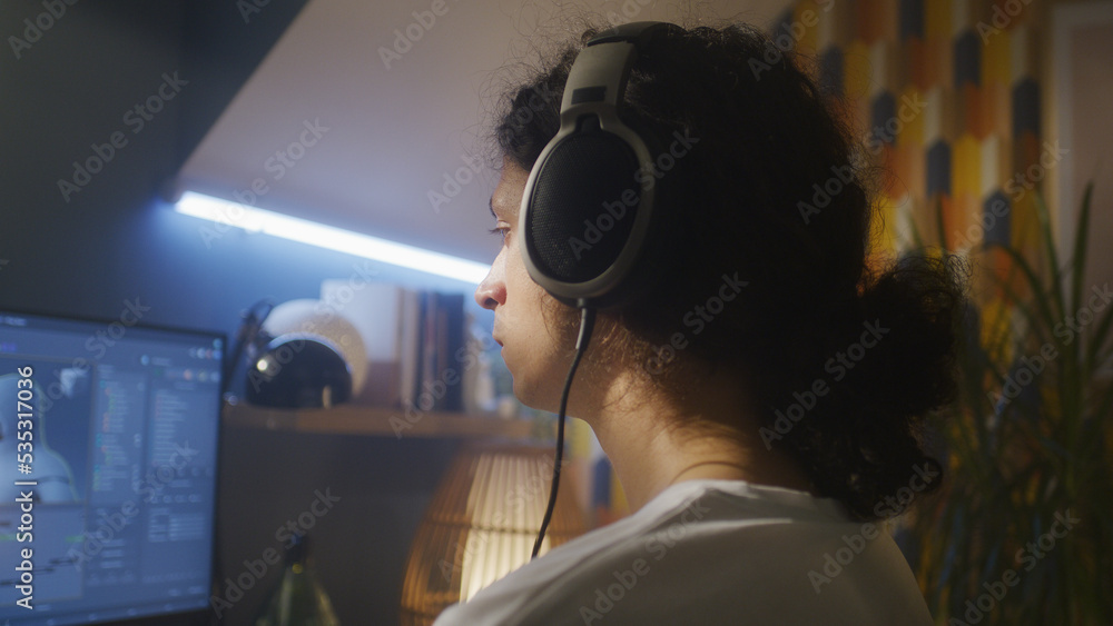 Poster Back view of man in headphones sitting at the table and creating video game hero and 3D animation in professional computer program, while working remotely at home.