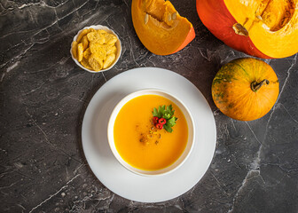 Autumn pumpkin cream soup with pumpkin spices. Delicious and bright vegetarian dish with foodstyling of fresh parsley with hot pepper and seasonings on a dark background. Menu concept, copy space