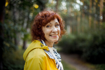 Portrait of a happy laughing elderly woman with red curly hair in the park.