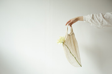 female hand holding a knitted bag with a white flower on a white background