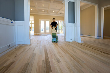 Carpenter grinding a wooden parquet floor by using floor sander in newly constructed house to...