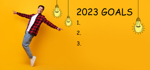 Happy millennial caucasian guy dancing, look at 2023 goals inscription with light bulbs, checklist