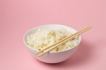 A plate of boiled rice and chopsticks on a pink background. traditional asian food