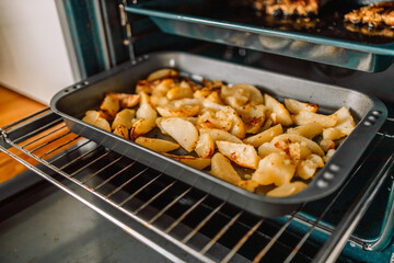 Woman taking hot roasted potatoes out of oven, closeup. High quality photo