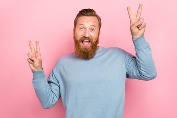 Photo of positive cheerful man with ginger hairdo dressed blue long sleeve showing v-sign say hi isolated on pink color background © deagreez